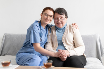 A female care worker and a woman sitting on a couch holding hands