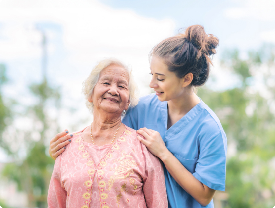 Smiling female care worker supports elderly woman outdoors, illustrating compassionate domiciliary care services