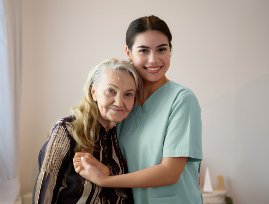 Smiling female care worker embraces elderly woman, illustrating compassionate personal care in elderly care