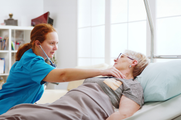 A female care worker using a stethoscope on an elderly woman lying in bed