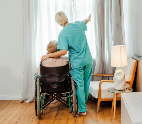 A female care worker and an elderly woman in a wheelchair looking out of the window together