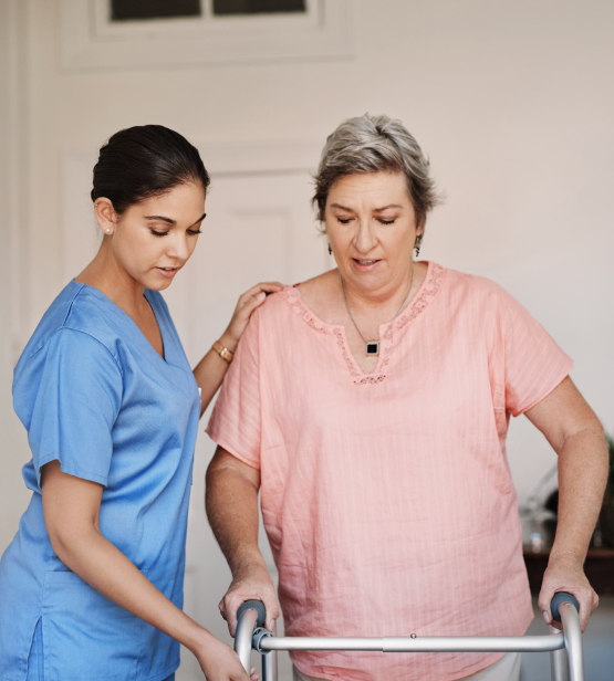 Female care worker supports elderly woman using walker, showcasing attentive domiciliary care services at home.