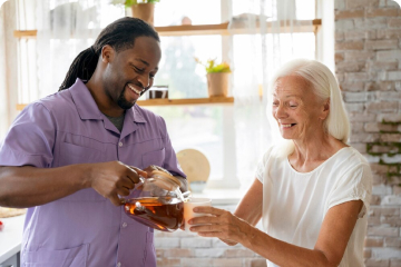 Smiling male care worker pours tea for cheerful elderly woman, depicting personalised specialist care at home