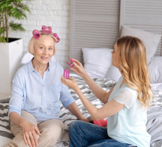 Female care worker styles elderly woman's hair with rollers, providing personal grooming in elderly care