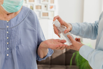 A  care worker sanitising the hand of an elderly person