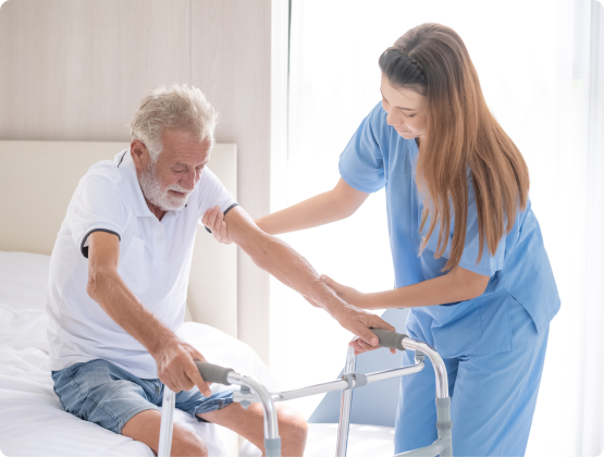 A female care worker helping an elderly man use a walker to stand from bed