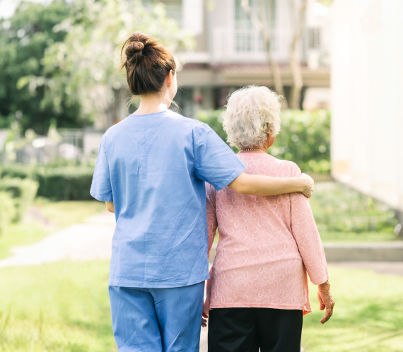 A female care worker walking with an elderly woman with her arm around her