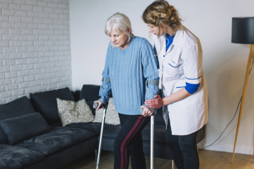 A female care worker helping an elderly woman with walking sticks in both hands